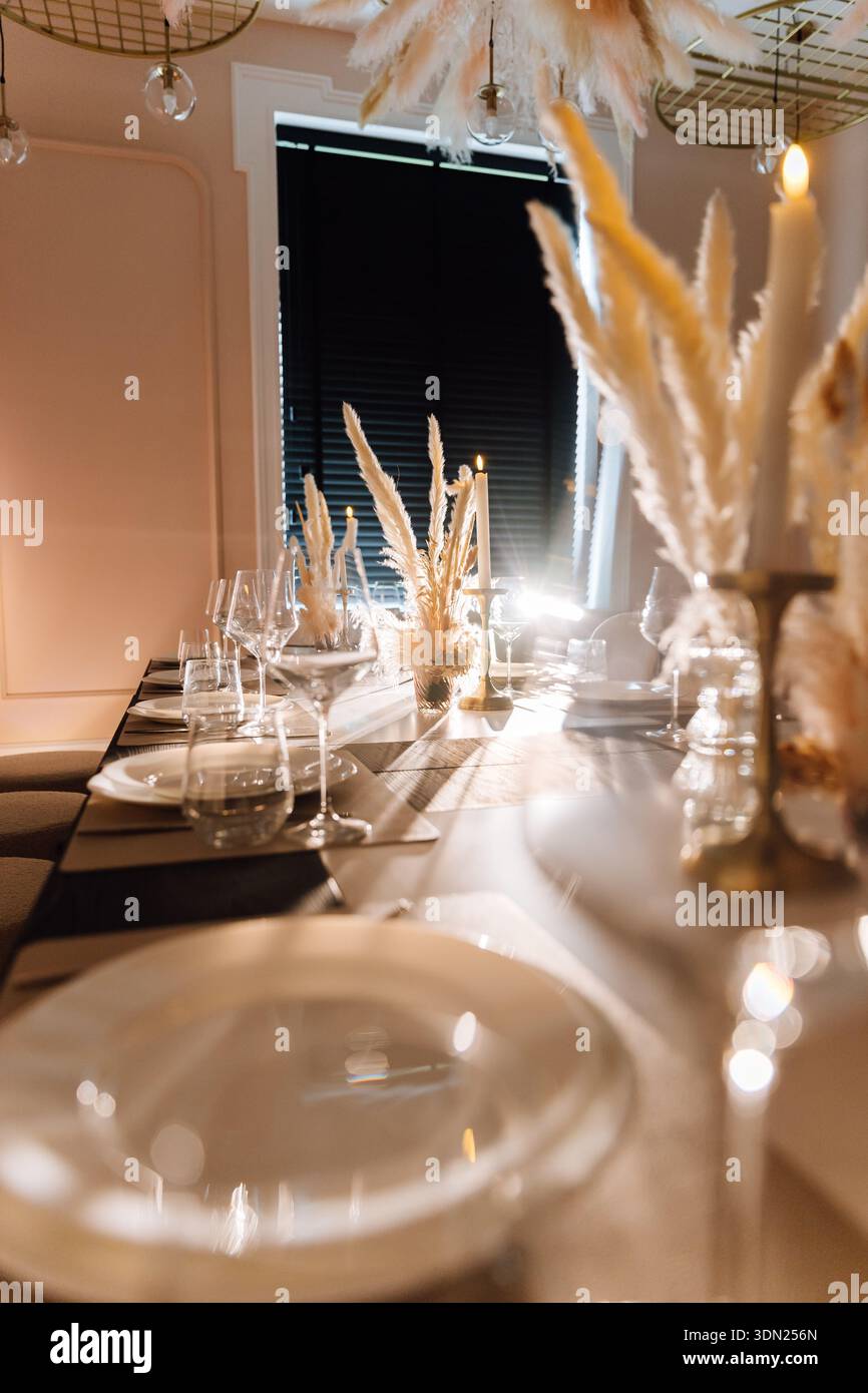 Candlelit restaurant table setting with pampas centerpiece and warm evening ambiance Stock Photo