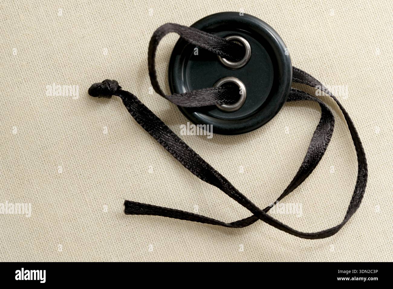 A delicate black button rests on soft fabric, tied with a graceful satin ribbon. Stock Photo
