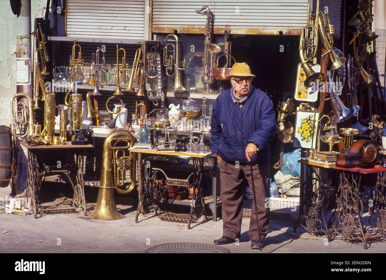 Greece, Athens A seller in his antique shop, stocked with various items, including brass instruments such as trumpets, trombones, and a tuba. Various Stock Photo