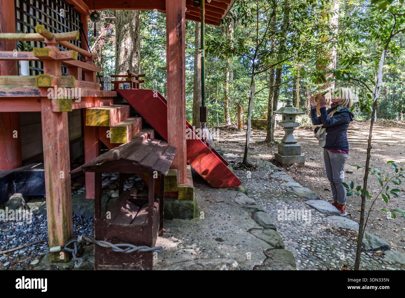 A pilgrim prays by a stone lantern at the Hosshinmon-oji shrine near Tanabe, Wakayama Prefecture, Japan. The site is the outermost gate to the sanctuary and the spiritual starting point of the final stage of the Nakahechi Route to Kumano Hongū Taisha. Stock Photo