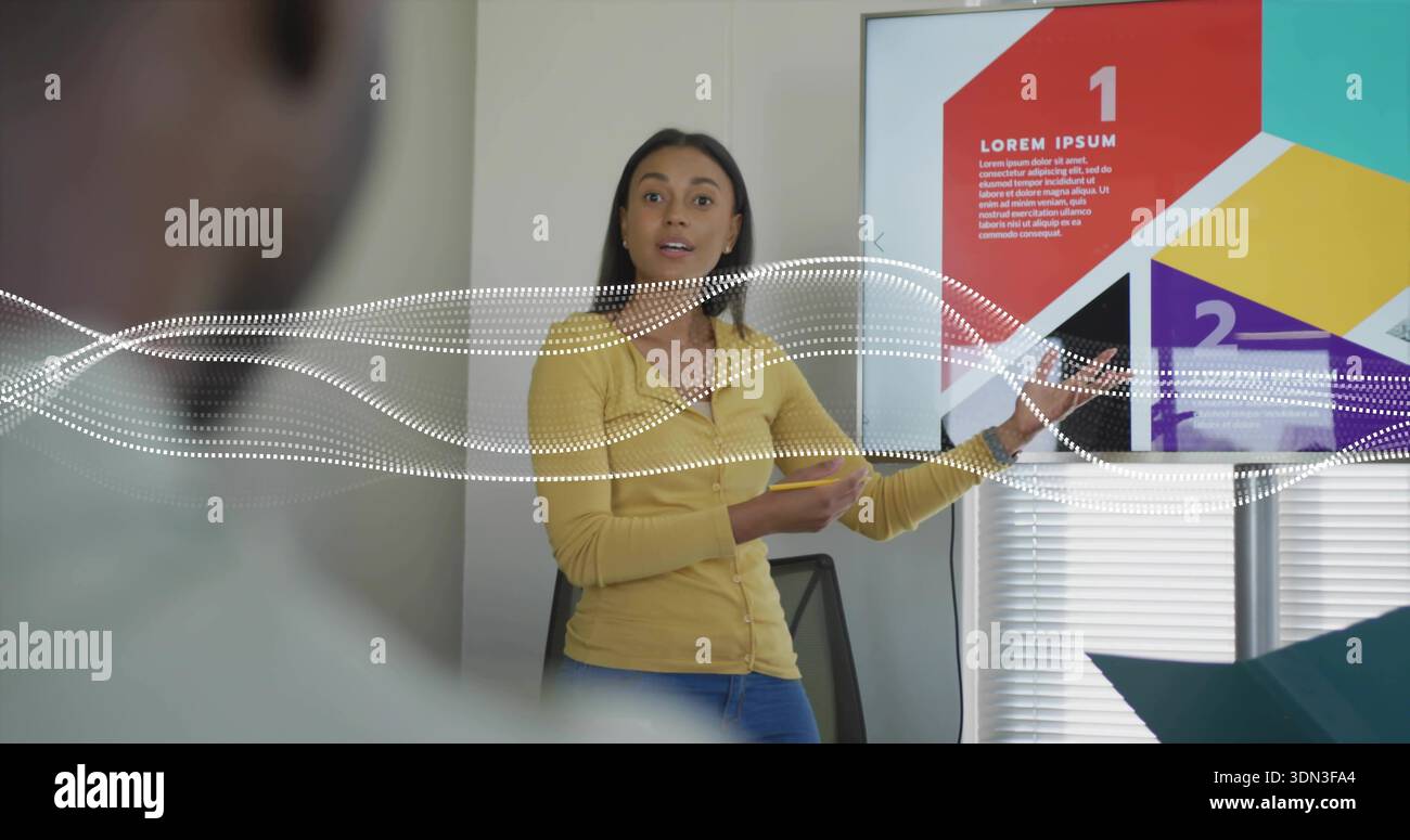 Talking woman in yellow cardigan, jeans pointing at display at office, numbered slide, teal folder Stock Photo