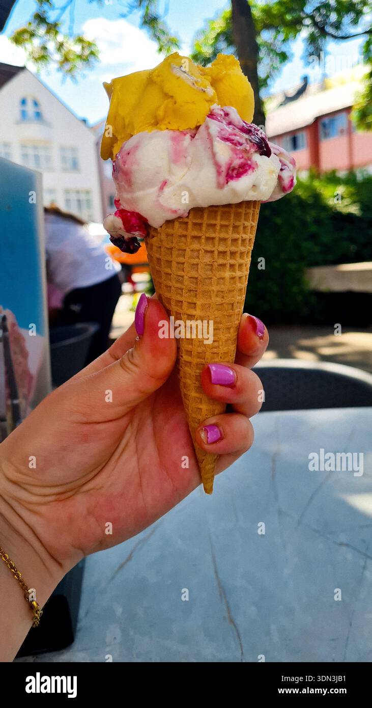 Close-up of a hand with purple nail polish holding an ice cream cone with two scoops Stock Photo
