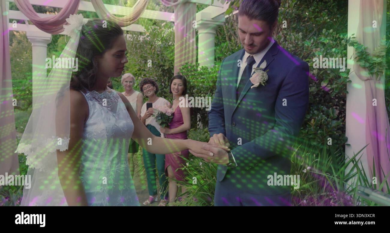 Placing groom placing ring on bride in lace gown and veil under garden ...