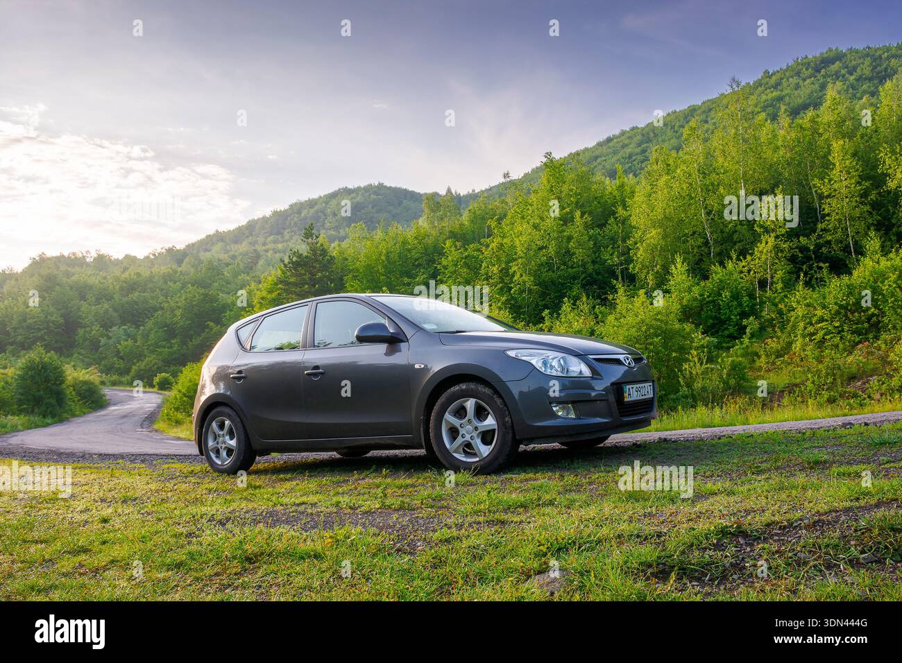 perechyn, ukraine - jun 10 2020: car near winding country road on summer sunrise. beautiful view of mountain in the background. automotive photography Stock Photo