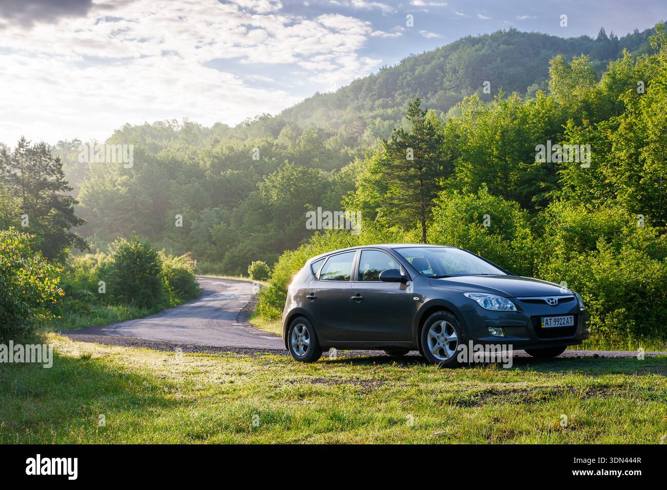 perechyn, ukraine - jun 10 2020: car near winding country road on summer sunrise. beautiful view of mountain in the background. automotive photography Stock Photo