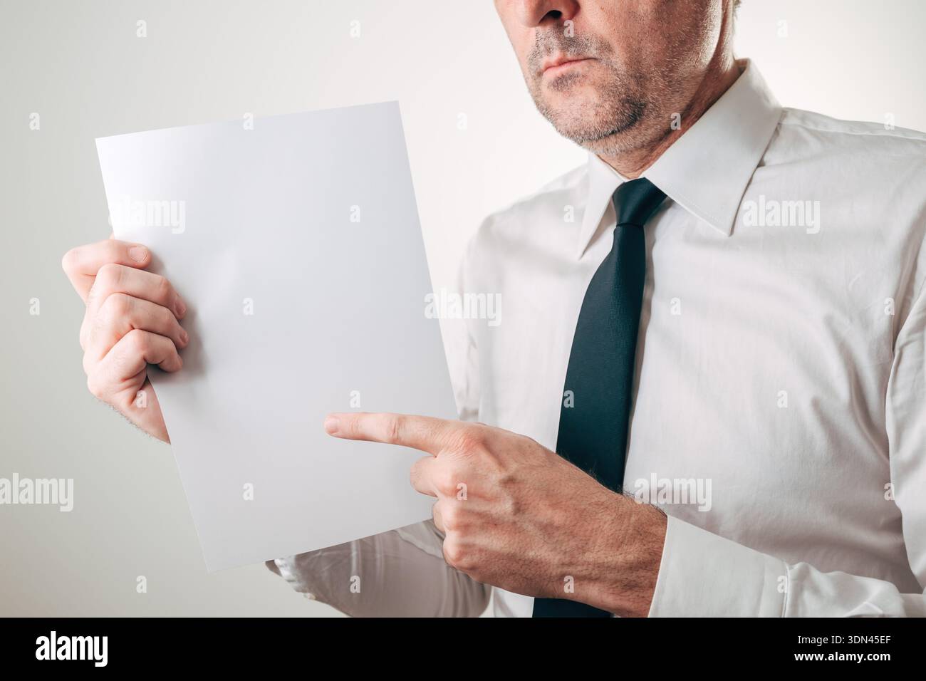 Serious businessman pointing at blank white paper sheet mockup, selective focus Stock Photo