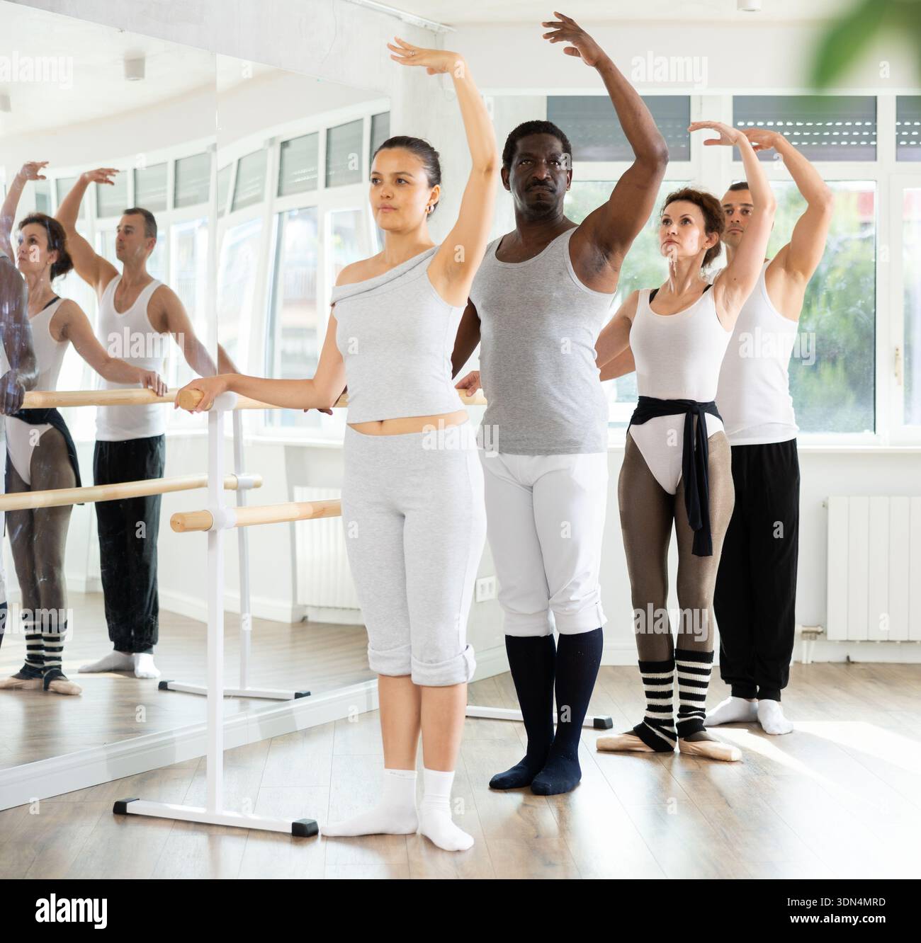 Group mastering third position at barre in ballet studio Stock Photo