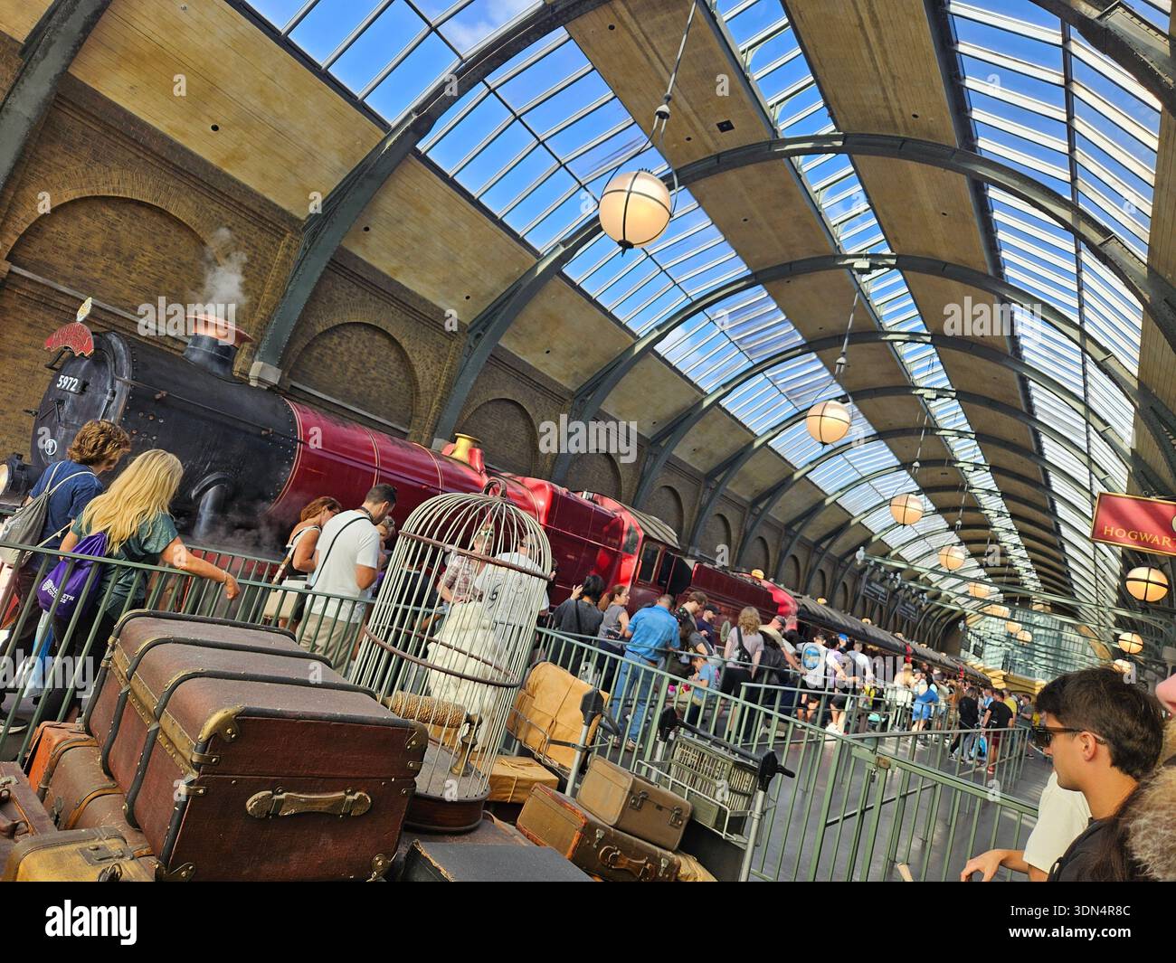 EDITORIAL USE ONLY-ORLANDO, FL-JANUARY, 2026: Tourists and fans gather at Platform 9 3/4 to board the Hogwarts Express train at King's Cross Station in Orlando Resort. The photograph shows the iconic red and black steam locomotive, vintage travel trunks, and an owl cage under the vaulted glass roof of the Wizarding World of Harry Potter. - Smartphone Captured Stock Image
