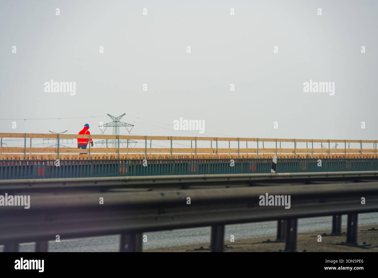 Construction worker in safety clothing walking along a bridge deck during a major infrastructure project showing human scale responsibility and precis Stock Photo