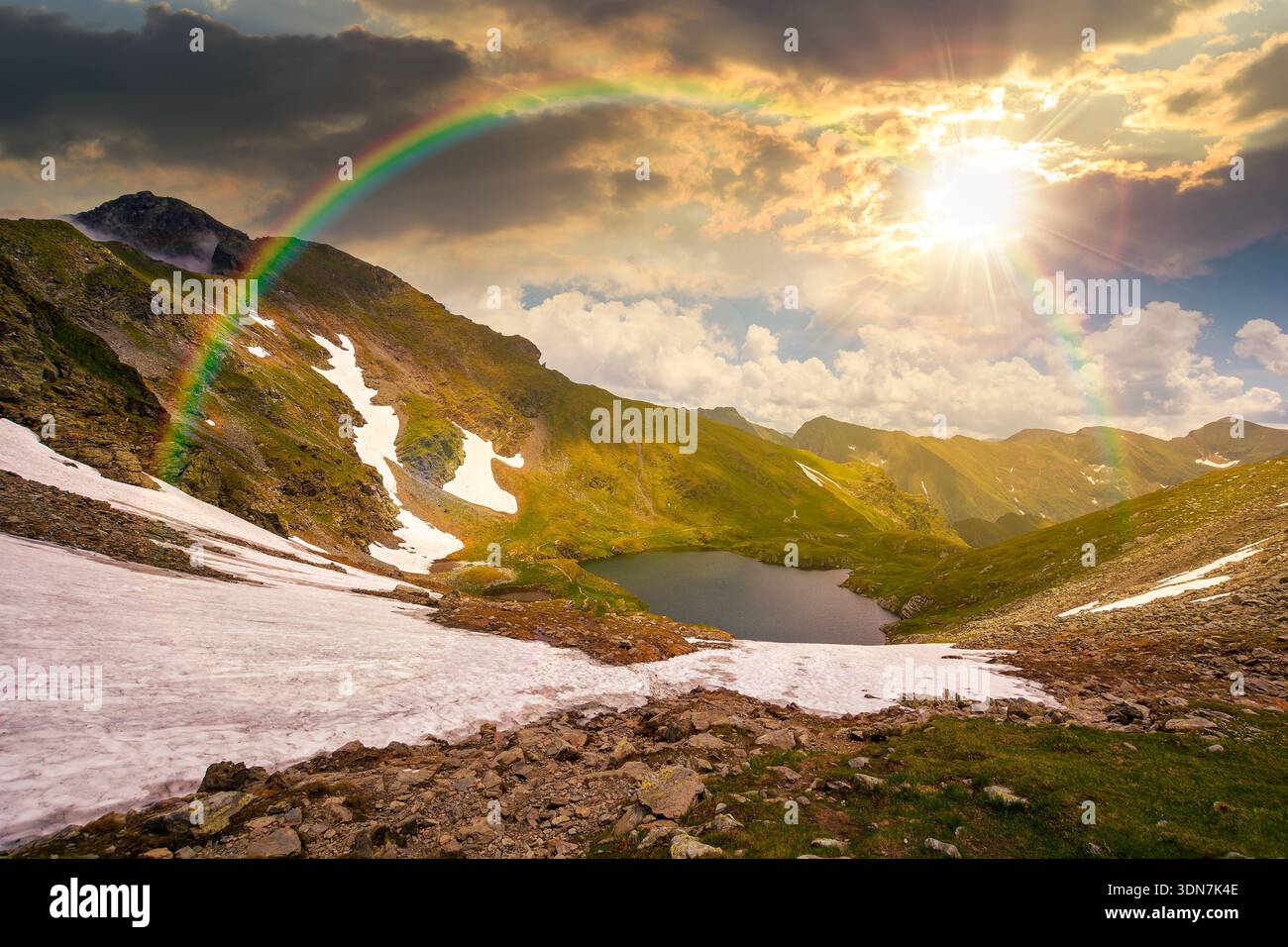 mountain lake in alpine summer landscape at sunset. beautiful view surrounded with clouds on a blue sky in evening light. fresh water, snow and rocky Stock Photo
