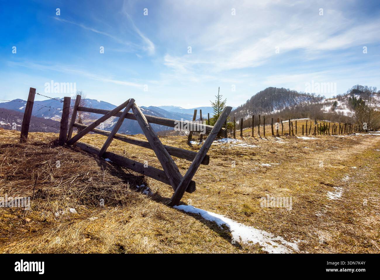 rural landscape of carpathian mountains in early spring under blue sky. snow covered hill with barbed wire fence on a sunny day. green environment sus Stock Photo