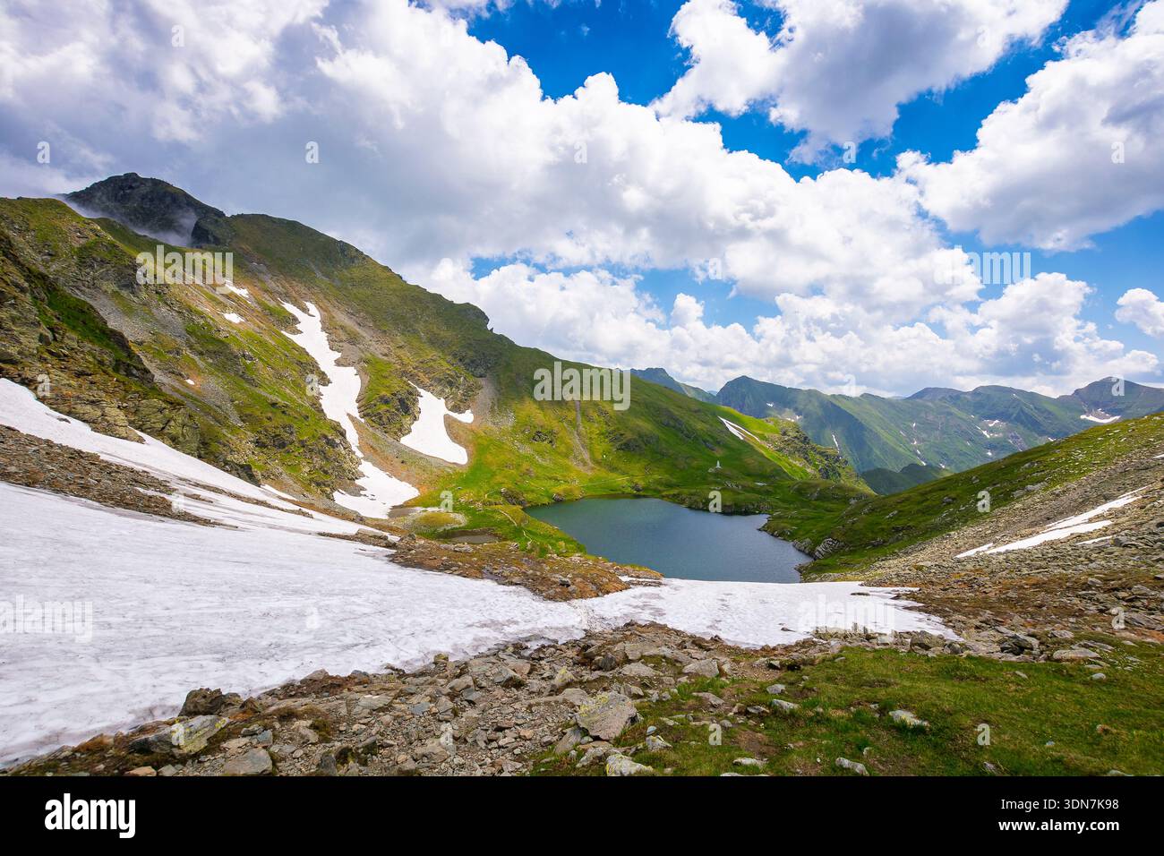 mountain lake in alpine summer landscape. beautiful view surrounded with transylvania alps and clouds on a blue sky. fresh water, snow and rocky slope Stock Photo