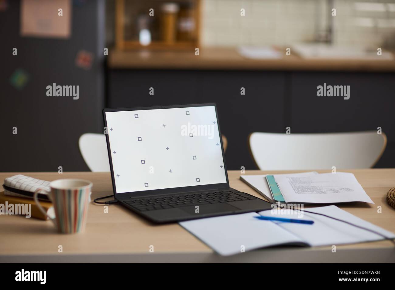 Open laptop with blank screen standing on kitchen table next to open notebook, pen, calculator and documents, suggesting remote work or study environment in modern home interior Stock Photo