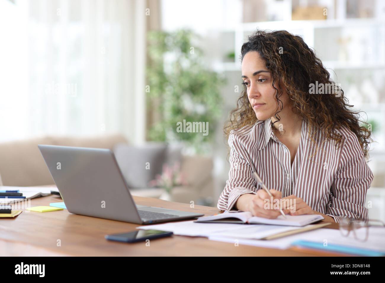 Adult freelance worker taking note in agenda checking laptop working at home Stock Photo