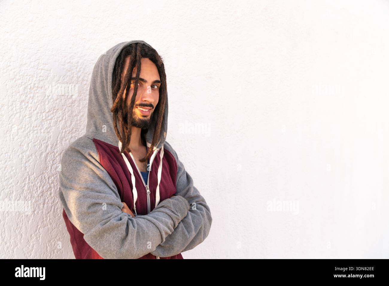 Young man with dreadlocks stands confidently against a white wall Stock Photo