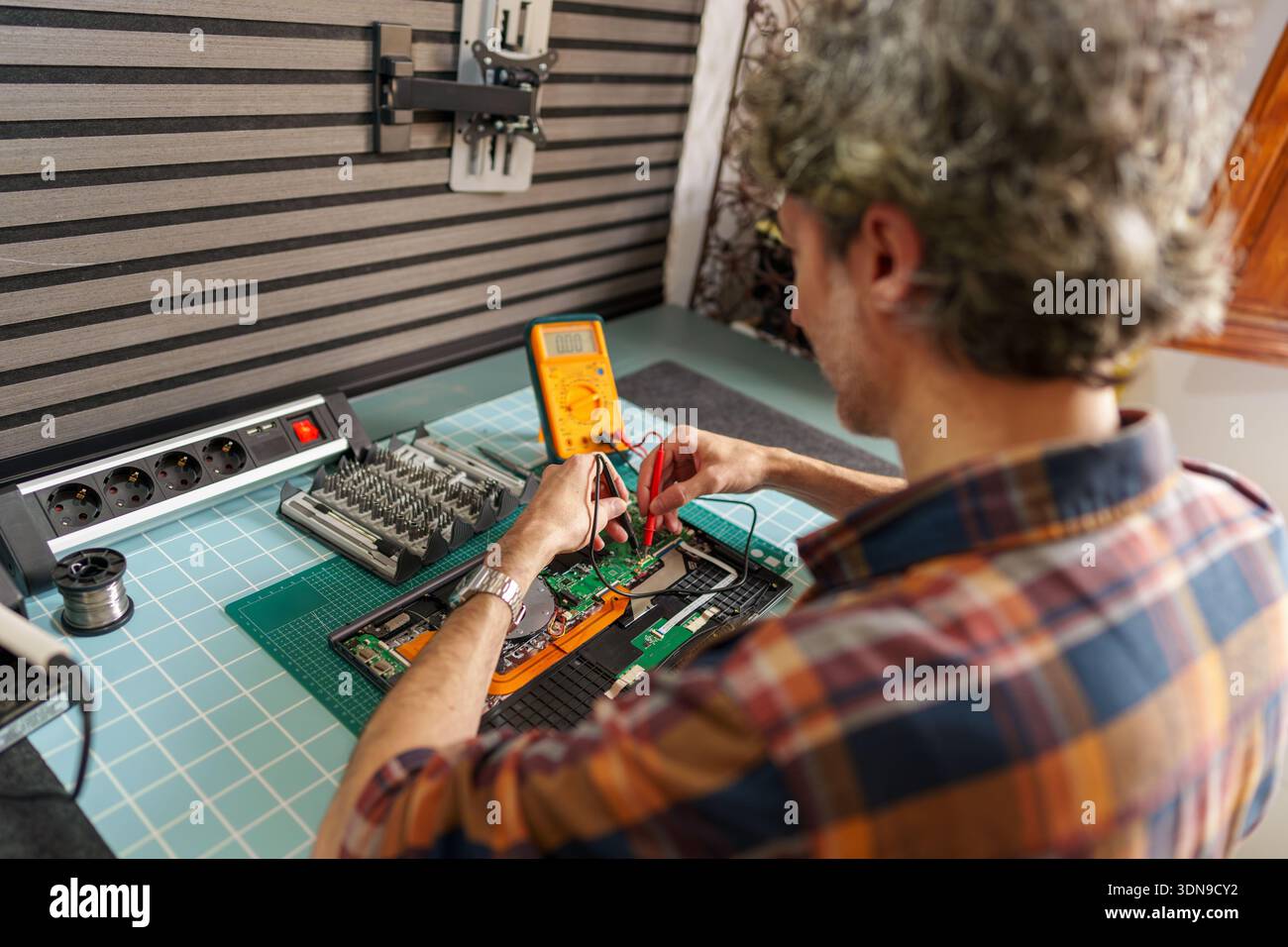 Technician checking electronic device circuit board with multimeter, diagnosing and repairing hardware problem Stock Photo