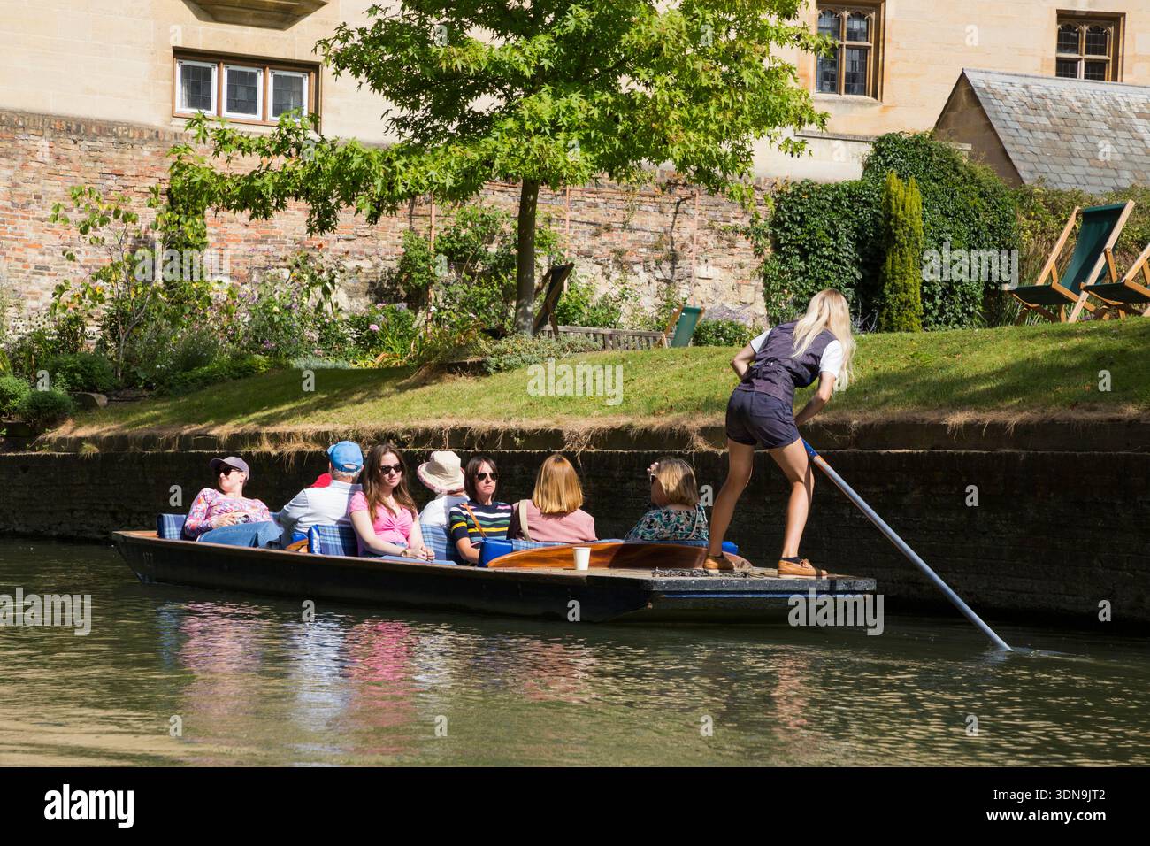 Woman female chauffeur / chauffeured group of visitors punting trip tourist punt boat trip for tourists around Cambridge on the river Cam; a sunny day with blue sky and sun. (138) Stock Photo