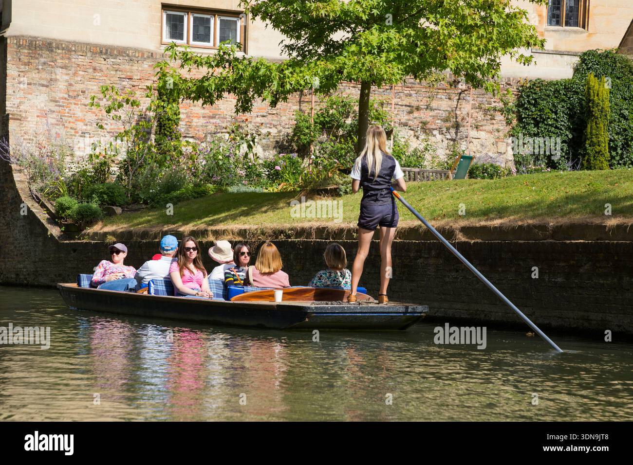 Woman female chauffeur / chauffeured group of visitors punting trip tourist punt boat trip for tourists around Cambridge on the river Cam; a sunny day with blue sky and sun. (138) Stock Photo
