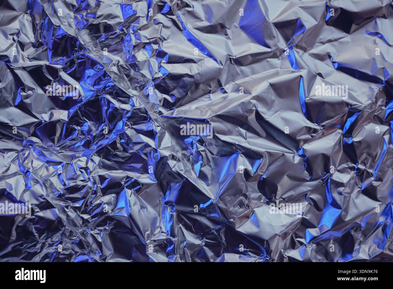 Wrinkled metallic texture creating an abstract pattern with silver and blue highlights Stock Photo