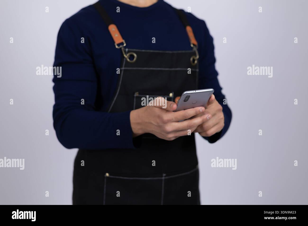 Service worker in apron using smartphone in studio Stock Photo