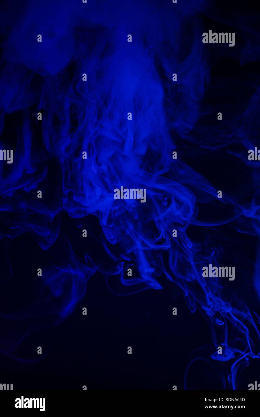 Thick curling blue smoke in dark environment Stock Photo