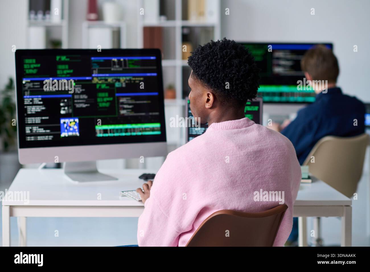 Young Black Man Writing Code on Computer in Office Setting Stock Photo