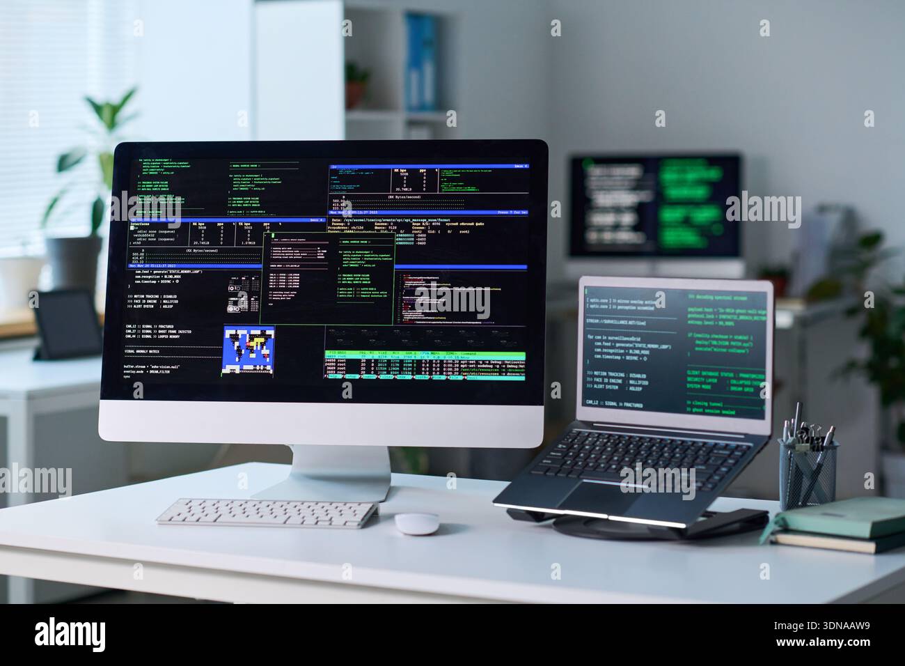 Office Desk Featuring Computer and Laptop Displaying Programming Code Stock Photo