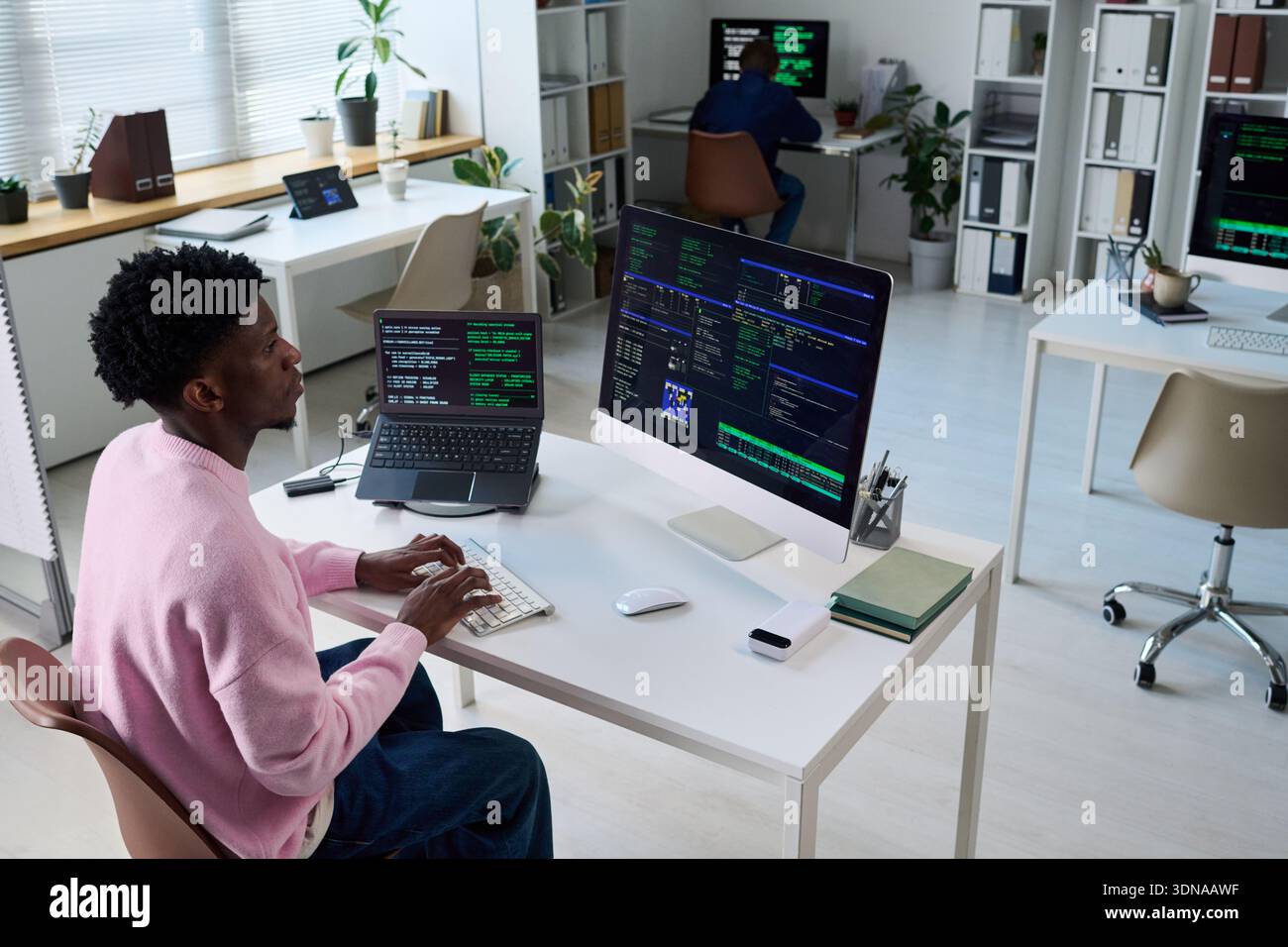 Young Black Man Coding on Computer in Office with Multiple Monitors Stock Photo