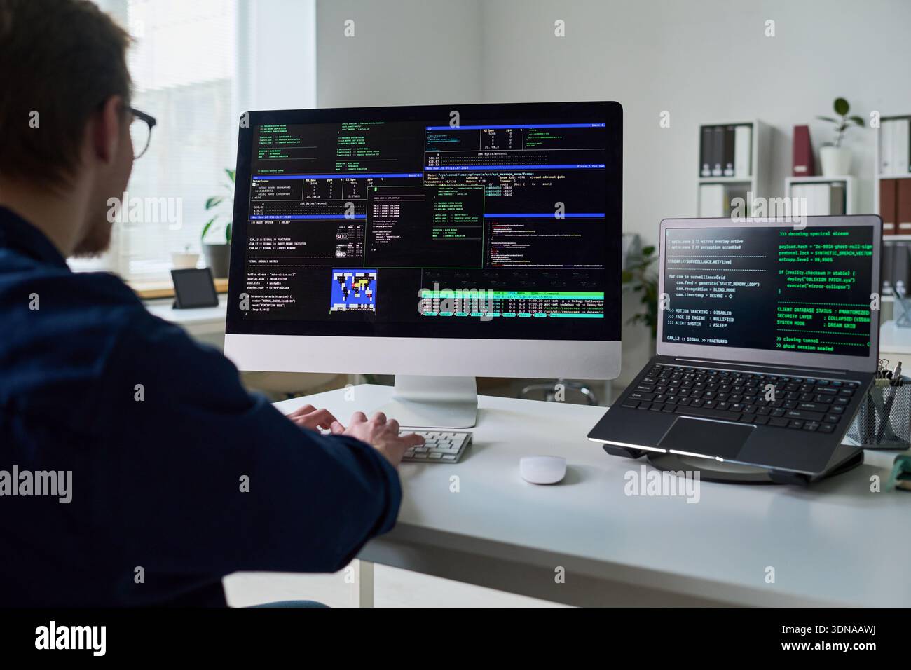Young Man Coding Software Applications on Desktop and Laptop Stock Photo