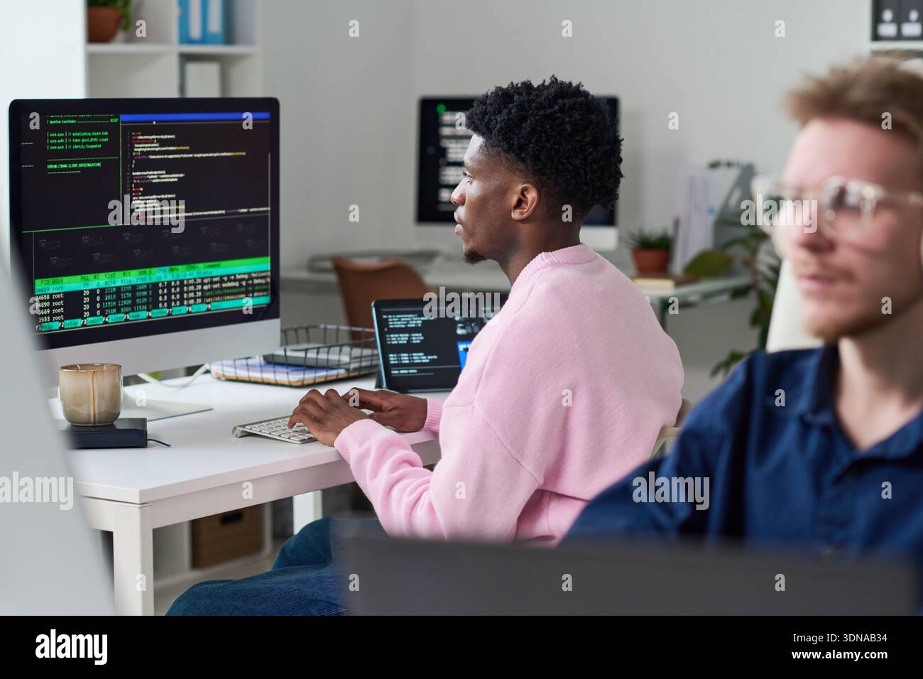 Young Black Man Debugging Software Code on Desktop Computer in Office Stock Photo