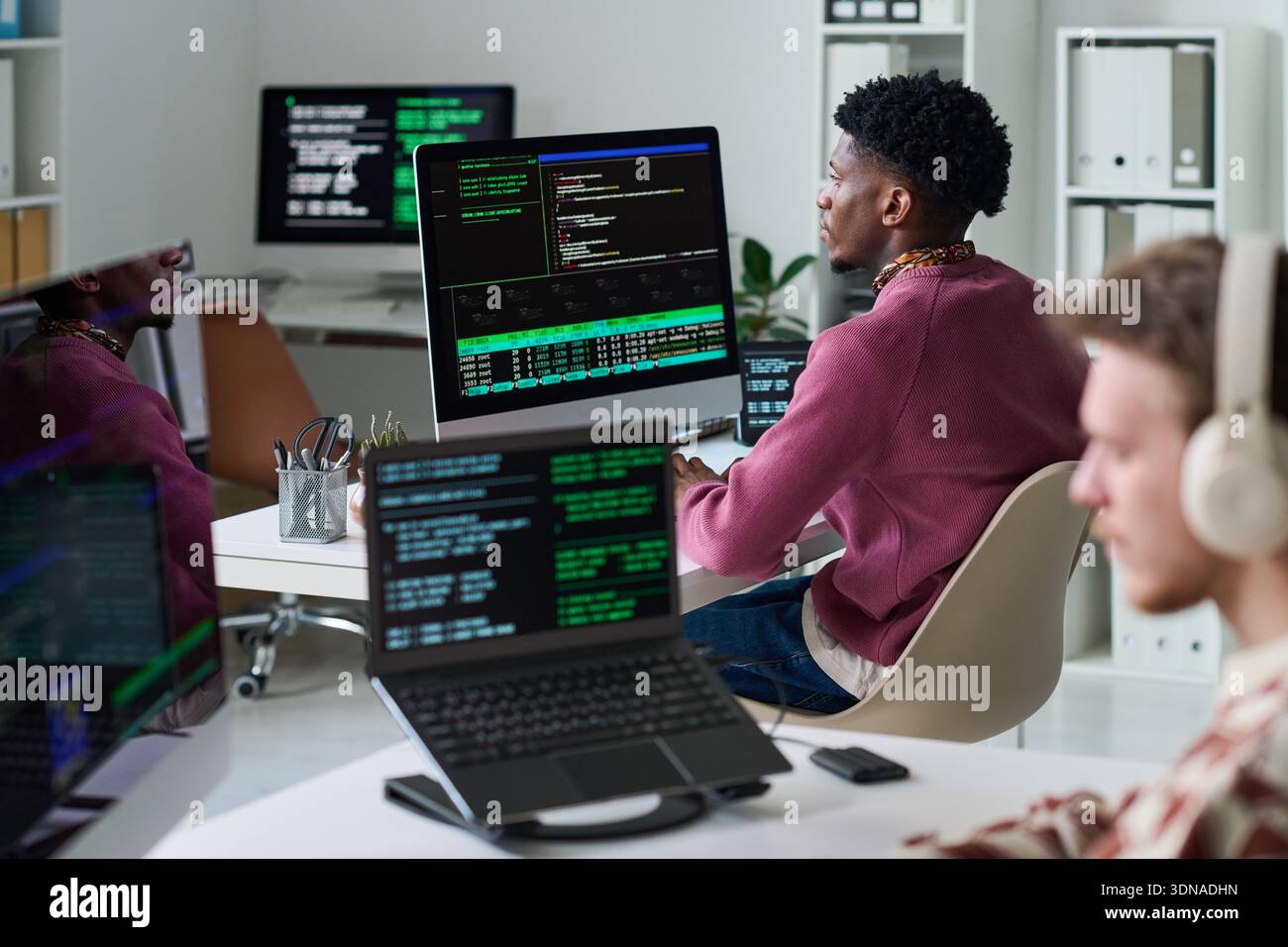 Young Black Man Reviewing Programming Code on Multiple Computer Screens Stock Photo