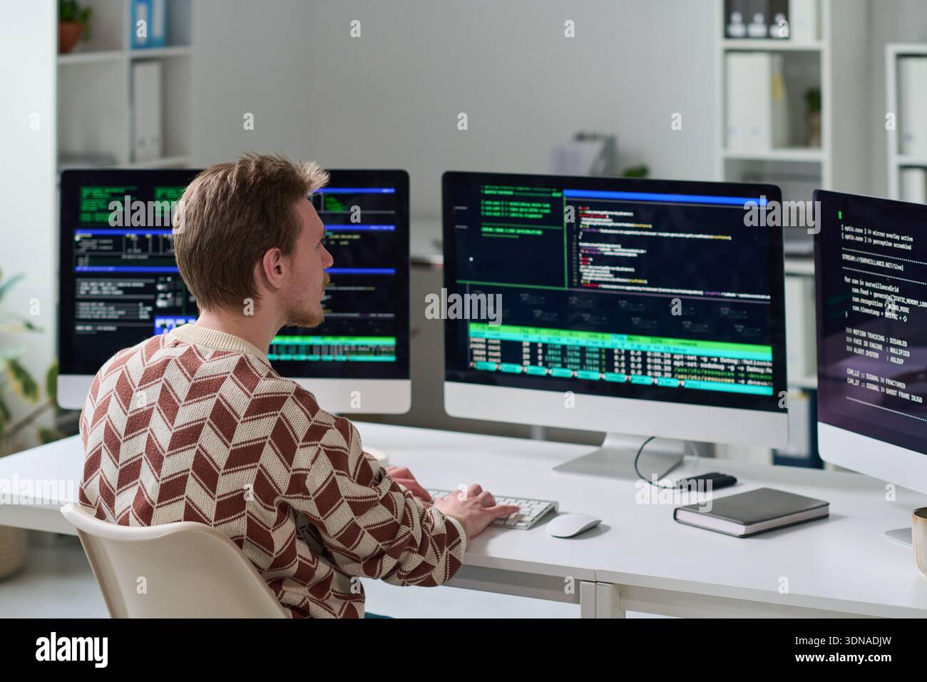 Young Man Working with Code on Multiple Computer Monitors Stock Photo
