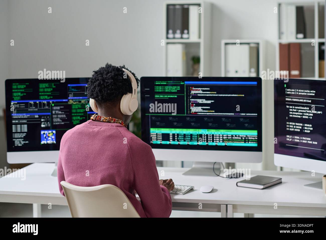 Young Black Man Wearing Headphones Coding Software on Multiple Monitors Stock Photo
