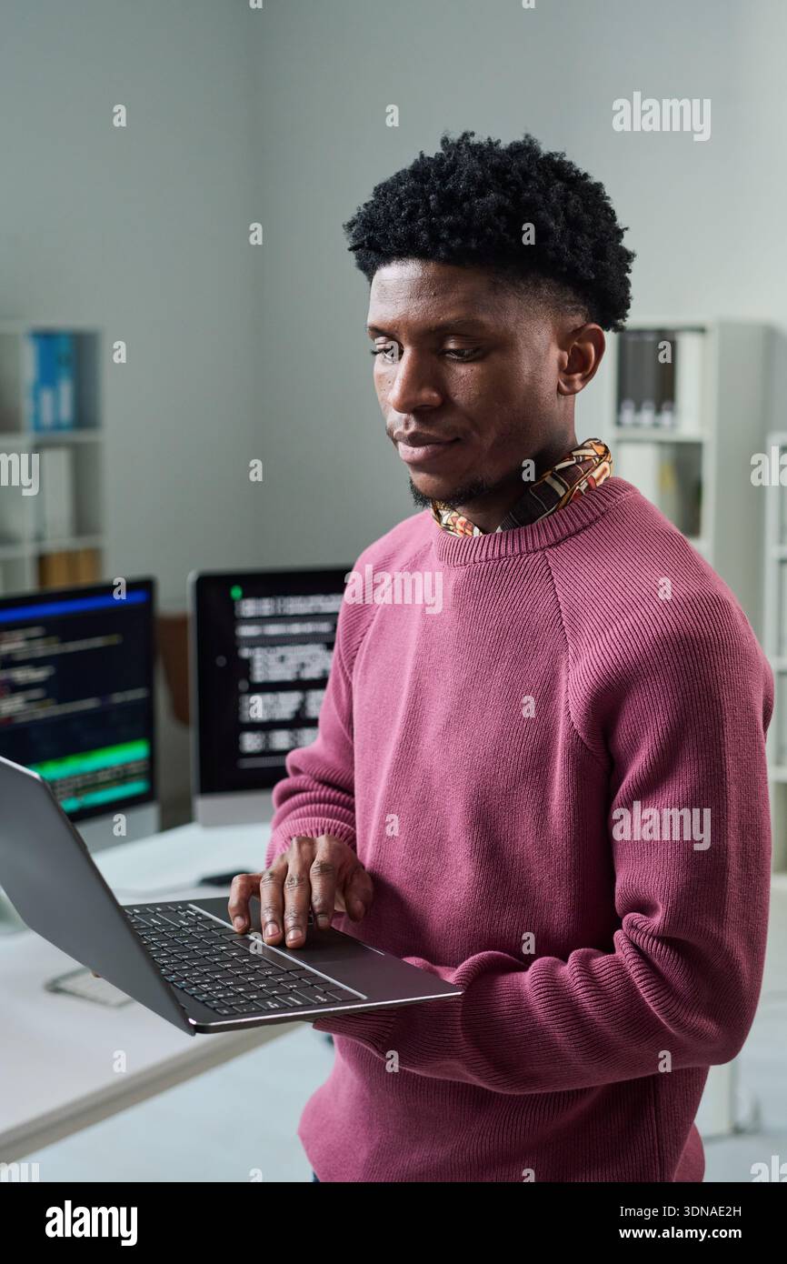 Young Black Man Using Laptop While Standing in Office Workspace Stock Photo