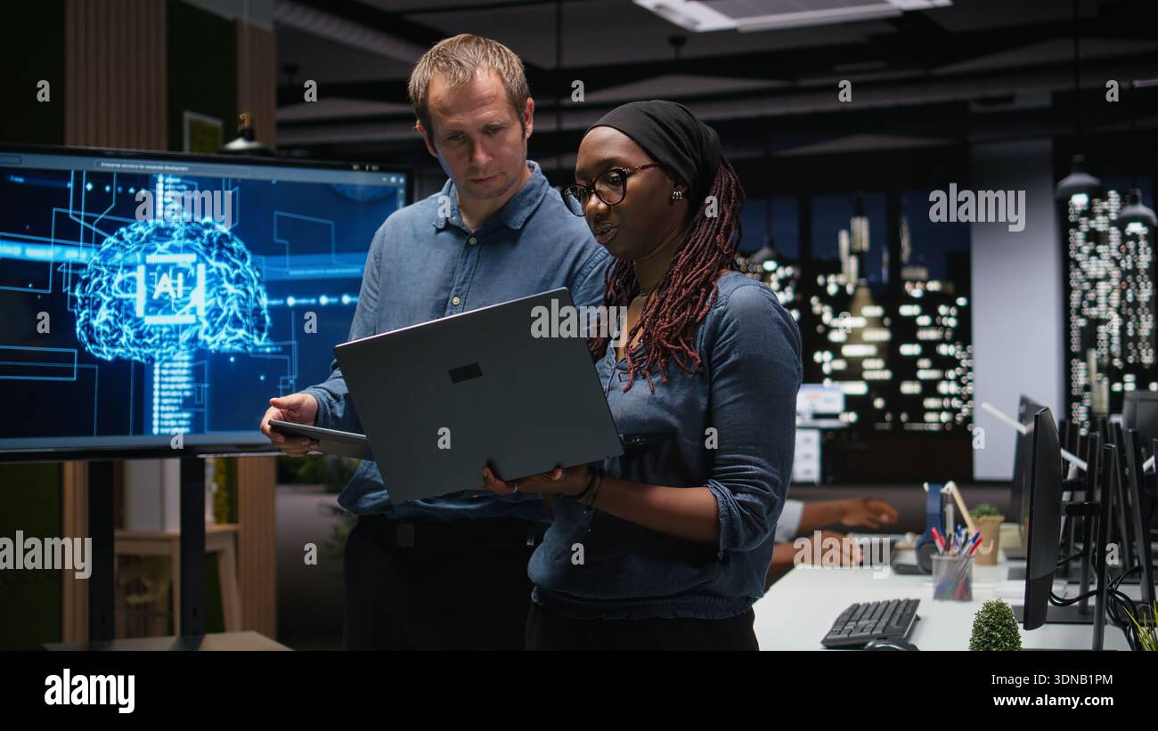 Engineering team in office analyzing machine learning algorithms using tablet and laptop. Coworkers discussing, using devices to improve artificial intelligence prediction accuracy Stock Photo