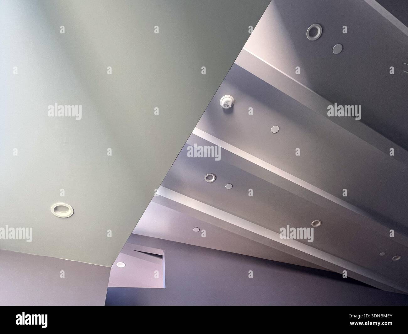 An abstract view of a low ceiling, a higher ceiling with its structural beams, a rnage of can lights, fire sprinkler heads, and a smoke detector, plus - Smartphone Captured Stock Image