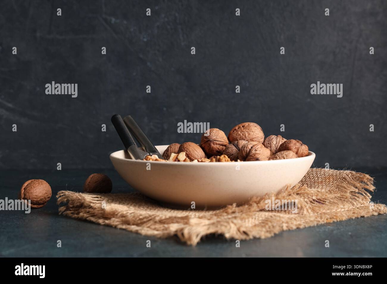 Bowl with tasty walnuts and nutcracker on dark background Stock Photo