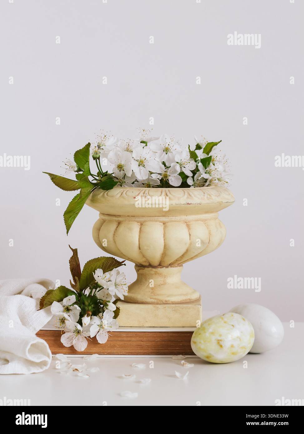 Spring composition with blooming cherry branches in a vase and decorative stone eggs on a bright background. Easter postcard with a copy space Stock Photo