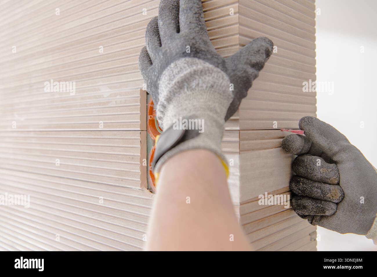 A person is installing ceramic tile panels in a home workshop while using tools and measuring carefully. Stock Photo