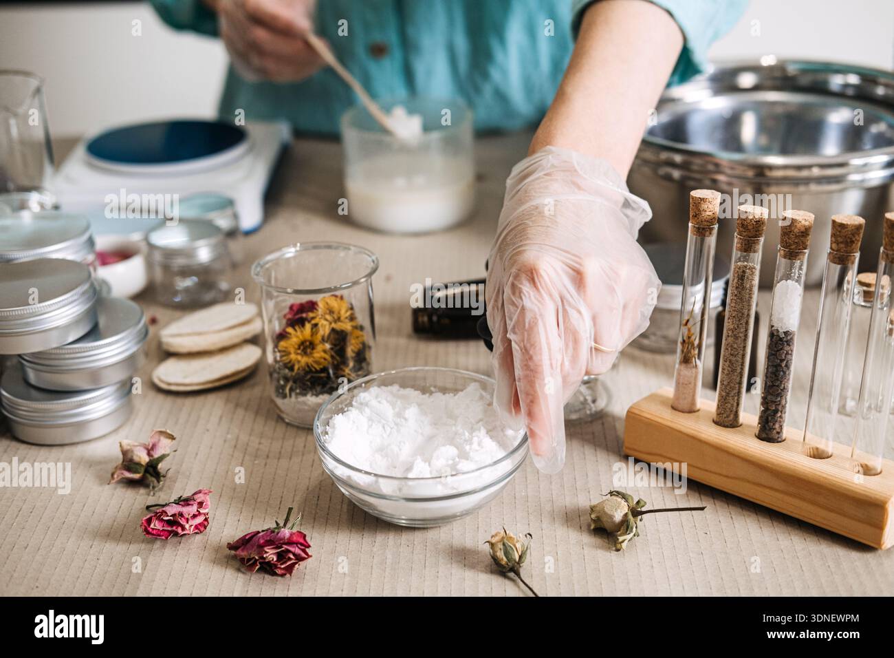 Hands wearing protective gloves scoop white powder into glass jar surrounded by apothecary supplies. slow beauty ritual, mindful skincare, calming DIY Stock Photo
