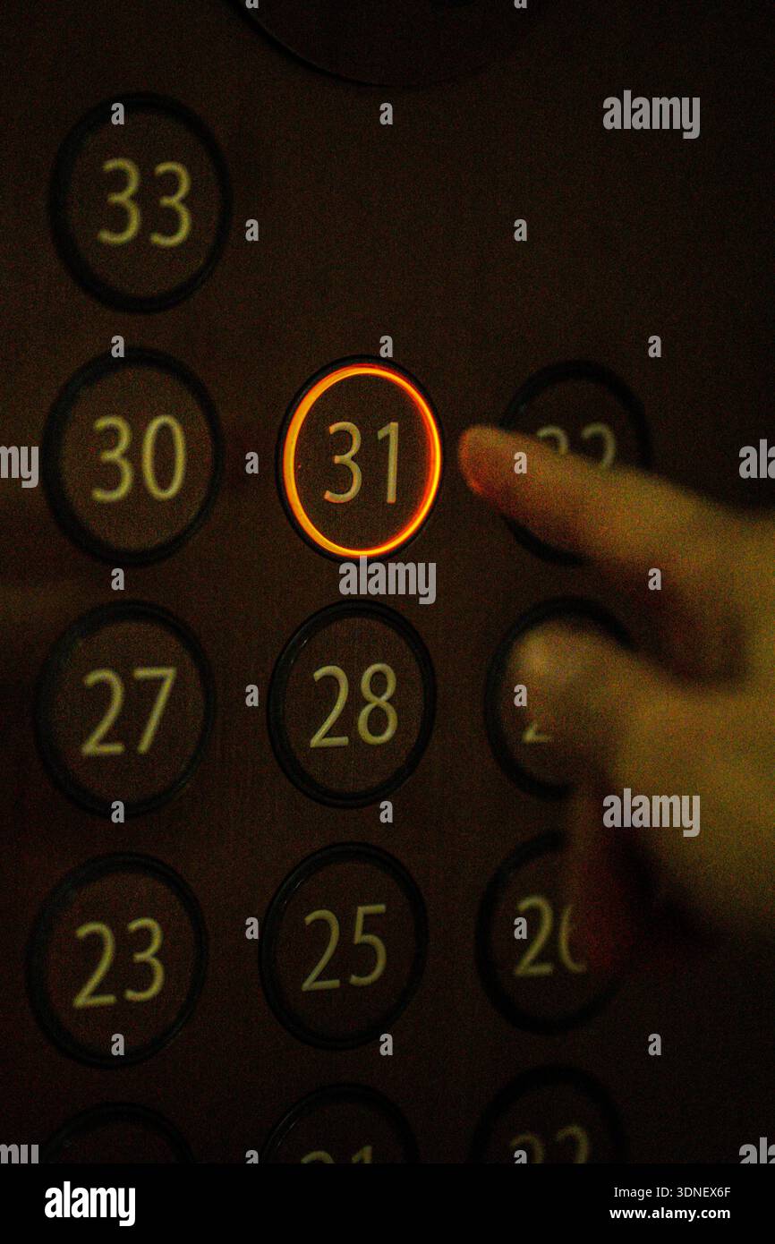 Hand pointing at highlighted number 31 on an elevator level panel, showing floor selection. Stock Photo