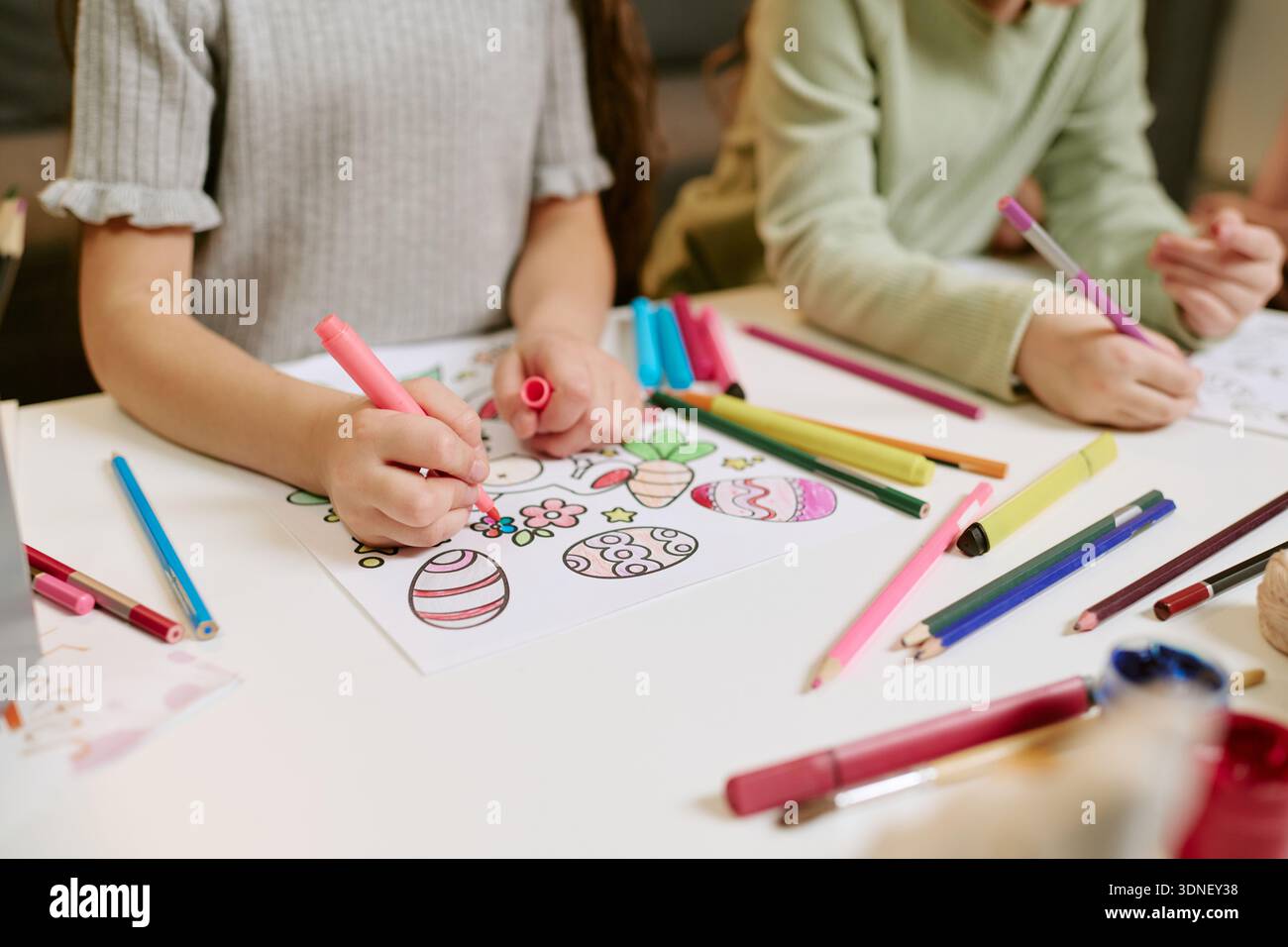 Girls Drawing Easter Eggs with Colored Markers at Table Indoors Stock Photo