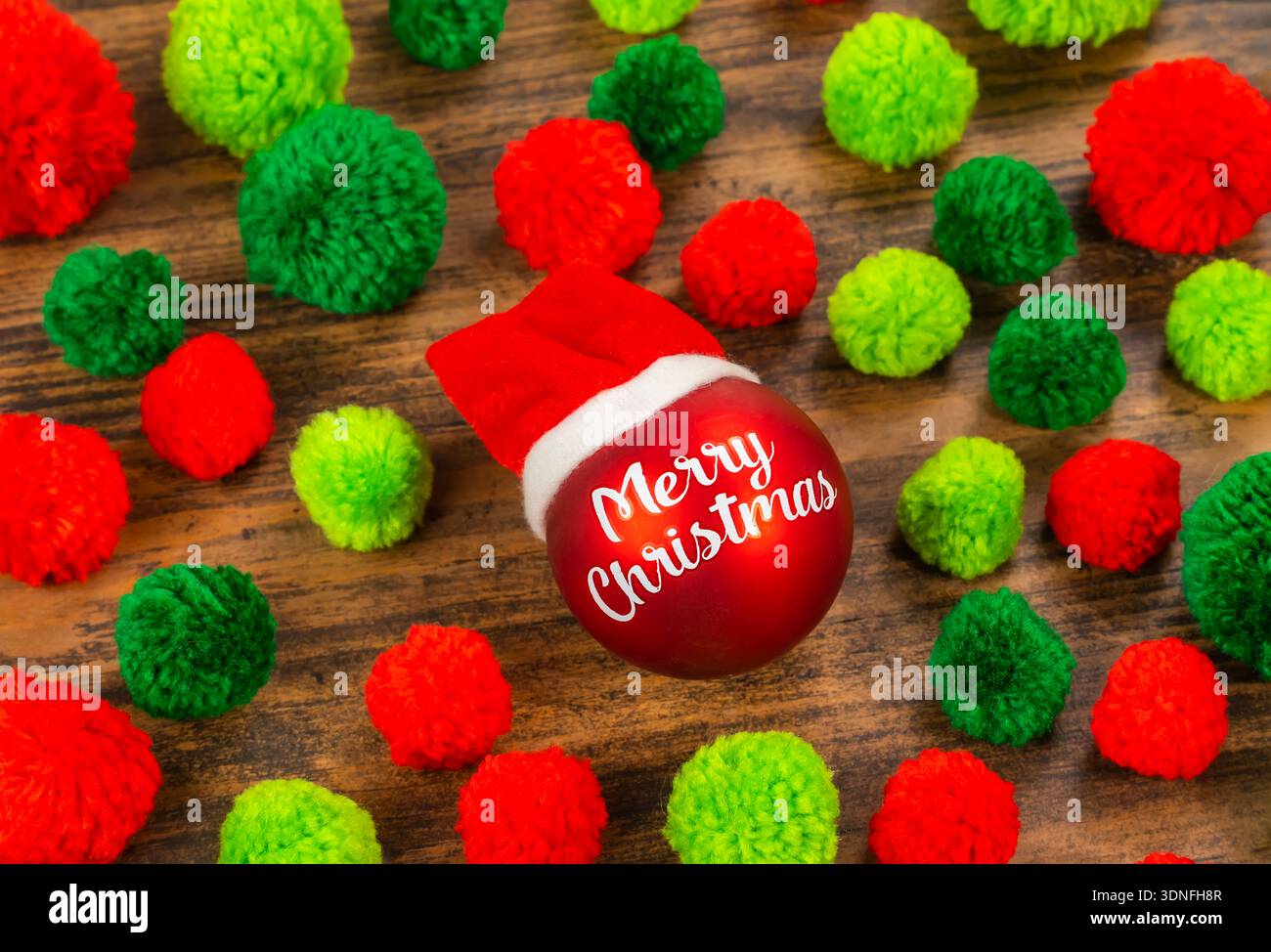 Red Christmas ball with words Merry Christmas on wooden background with pompoms Stock Photo