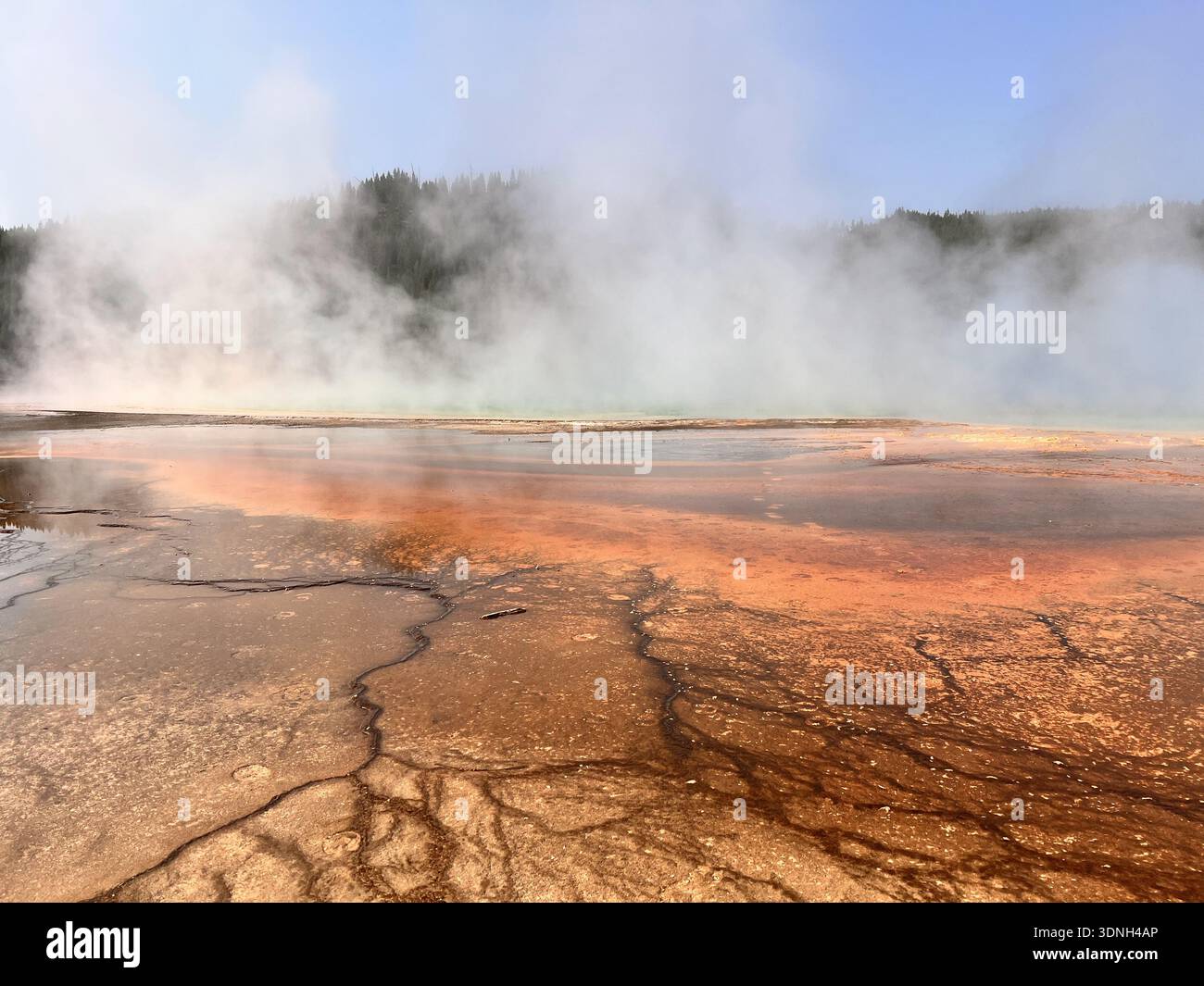 Steam rises from vivid orange and red mineral deposits in a geothermal landscape, creating a dramatic and colorful scene framed by hills and clear sky - Smartphone Captured Stock Image