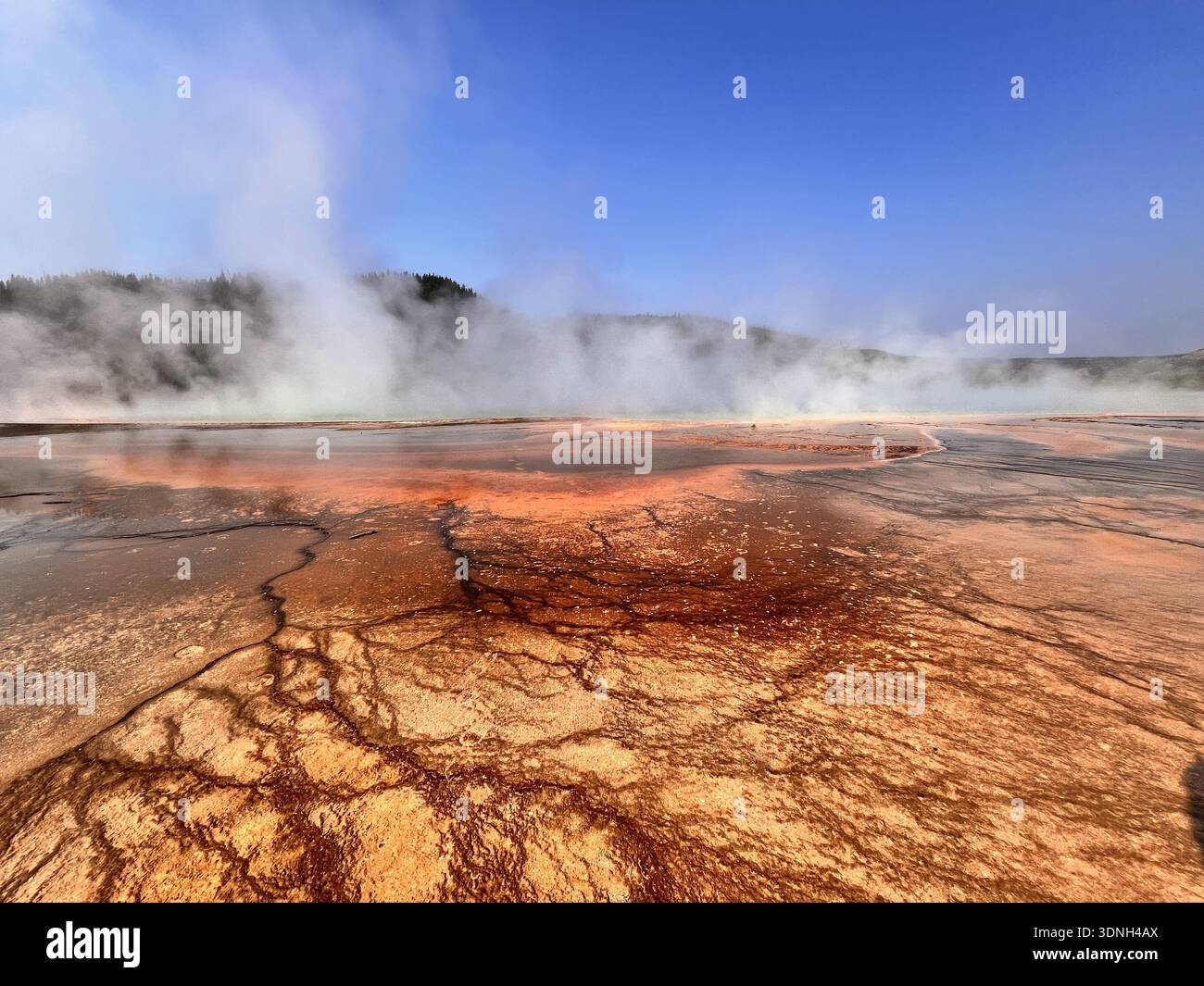 Steam rises from vivid orange and red mineral deposits in a geothermal landscape, creating a dramatic and colorful scene framed by hills and clear sky - Smartphone Captured Stock Image