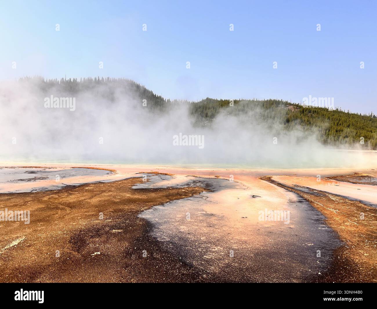 Steam rises from vivid orange and red mineral deposits in a geothermal landscape, creating a dramatic and colorful scene framed by hills and clear sky - Smartphone Captured Stock Image