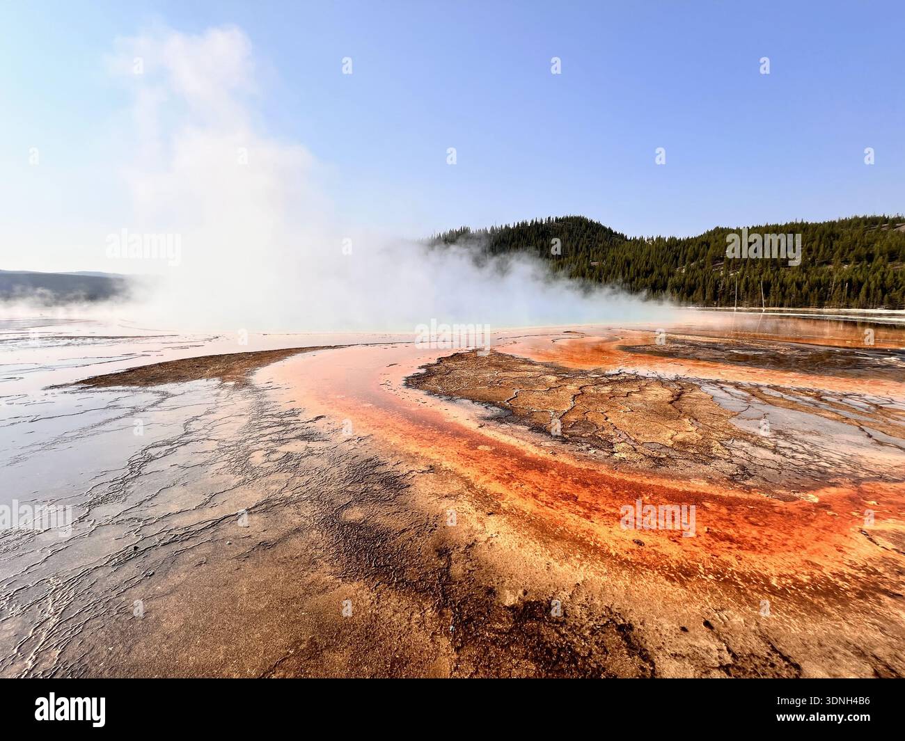 Steam rises from vivid orange and red mineral deposits in a geothermal landscape, creating a dramatic and colorful scene framed by hills and clear sky - Smartphone Captured Stock Image