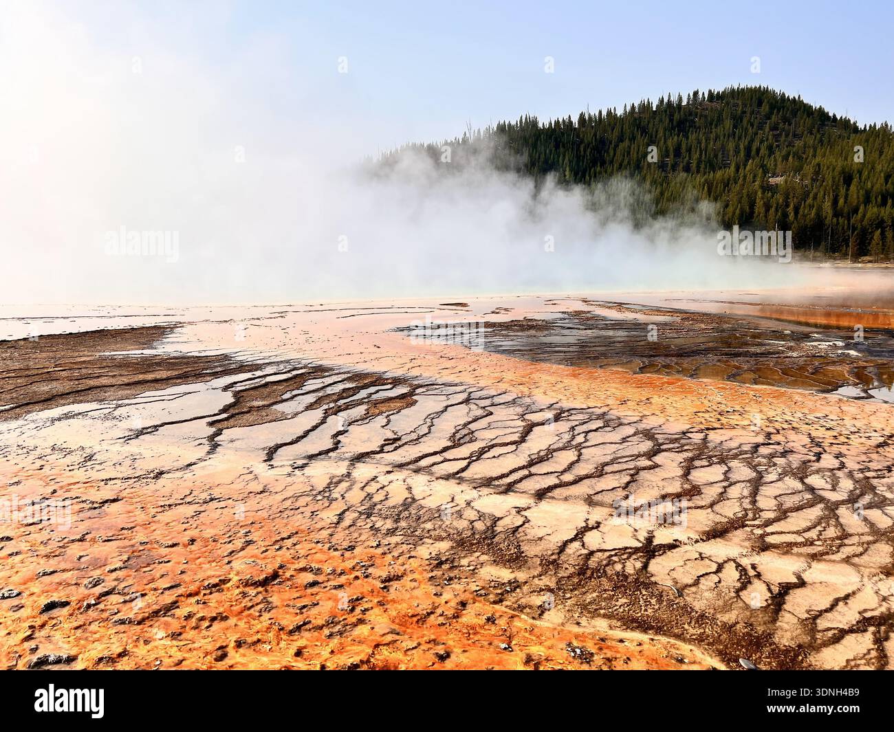 Steam rises from vivid orange and red mineral deposits in a geothermal landscape, creating a dramatic and colorful scene framed by hills and clear sky - Smartphone Captured Stock Image