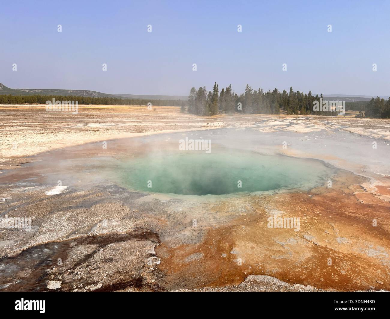 Steam rises from vivid orange and red mineral deposits in a geothermal landscape, creating a dramatic and colorful scene framed by hills and clear sky - Smartphone Captured Stock Image