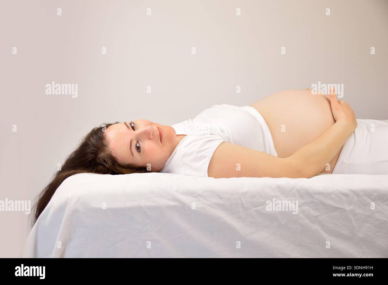 Pregnant woman lying down on a bed at home Stock Photo